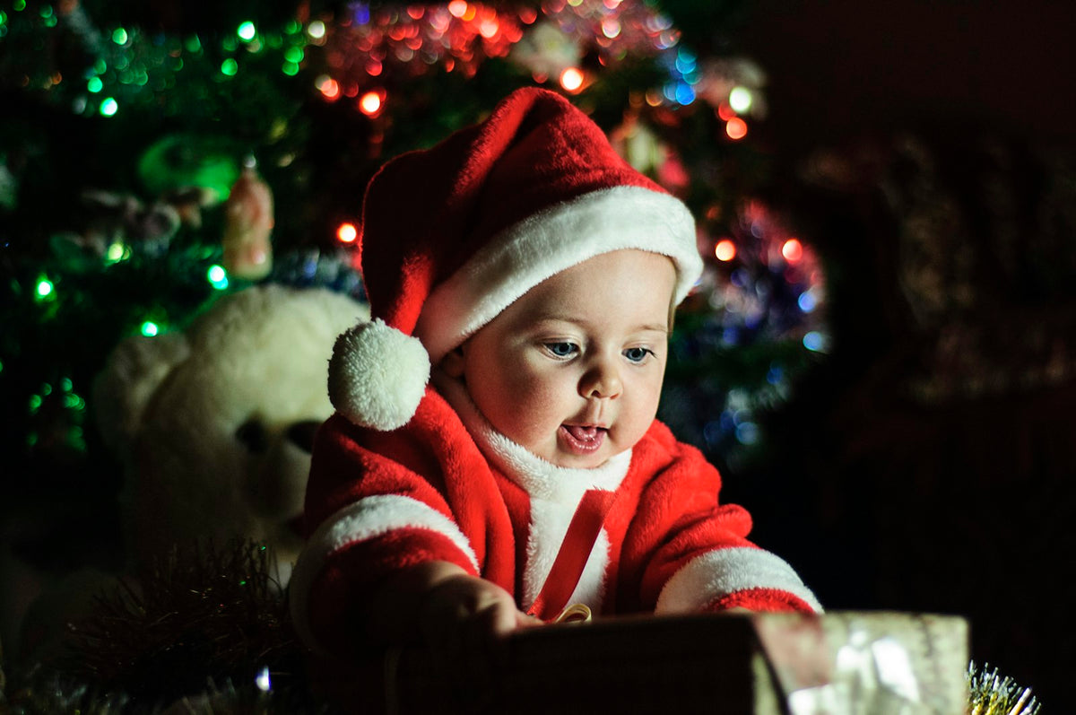 Baby in a Santa outfit next to a Christmas tree, celebrating baby's first Christmas