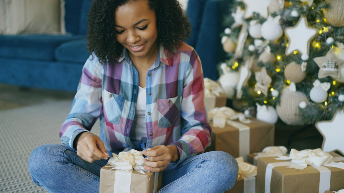 Wife smiling as she opens a Christmas gift by the tree