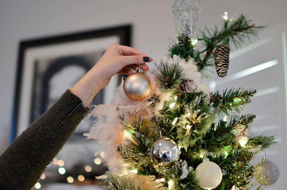 Hand hanging an ornament on a family Christmas tree, personalized family Christmas ornaments guide