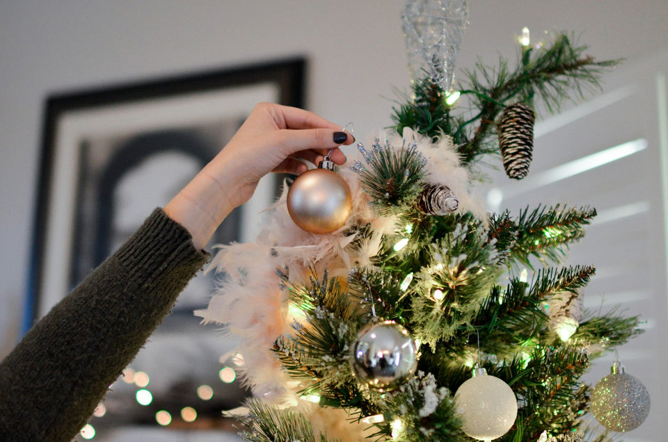 Hand hanging an ornament on a family Christmas tree, personalized family Christmas ornaments guide