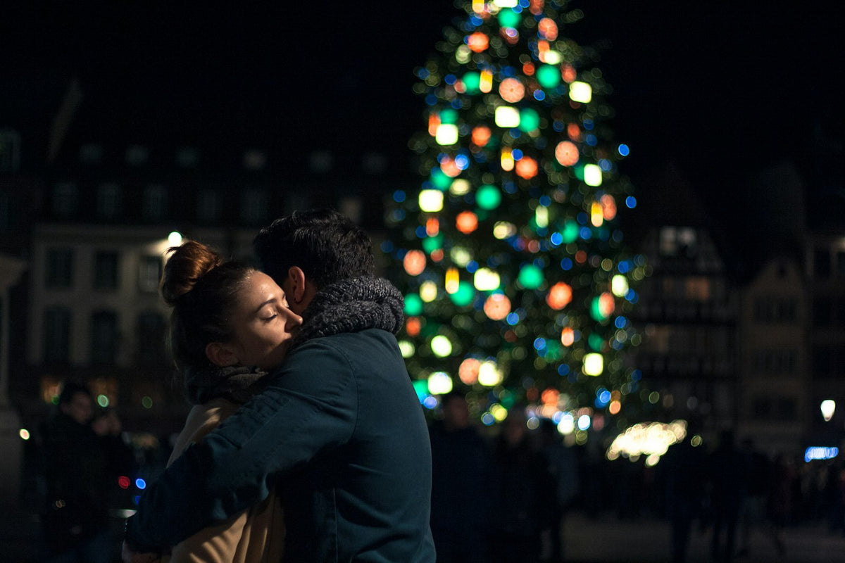 Couple hugging beside a lit Christmas tree, Christmas gifts for couples
