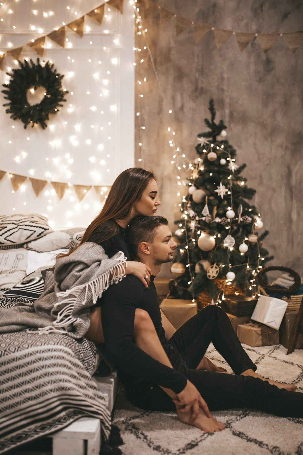 Engaged couple sitting beside a Christmas tree, ready to hang their engagement Christmas ornament