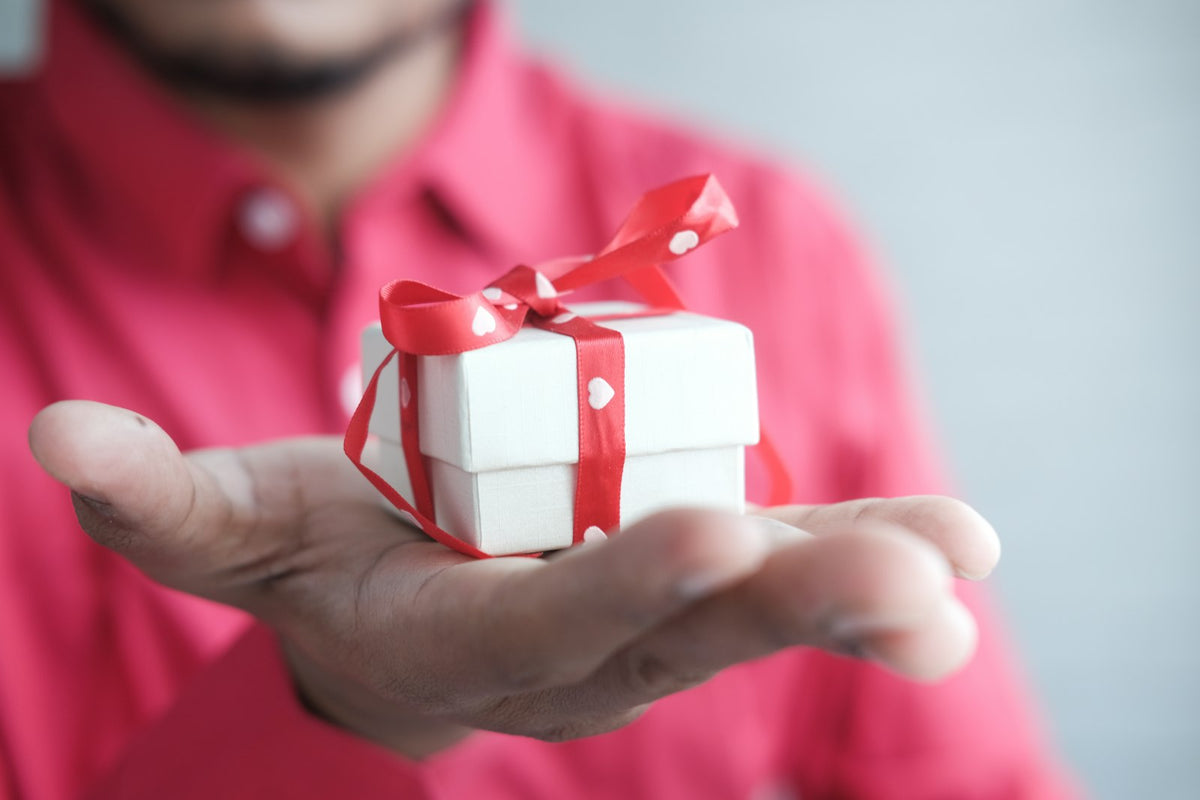 Man holding a white gift box with a red ribbon, a Christmas gift for men
