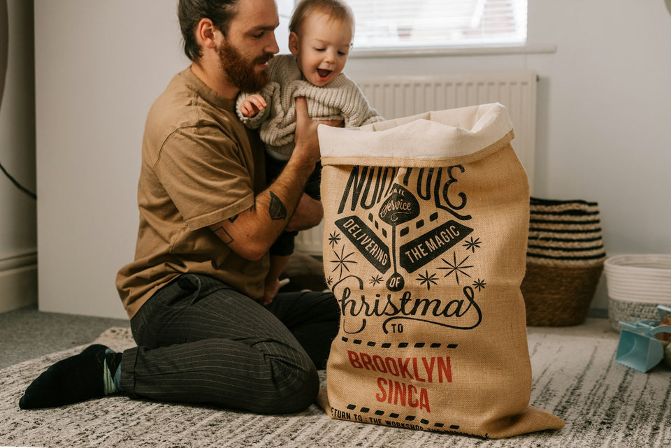 Dad sitting by the Christmas tree with his baby, opening Christmas gifts together