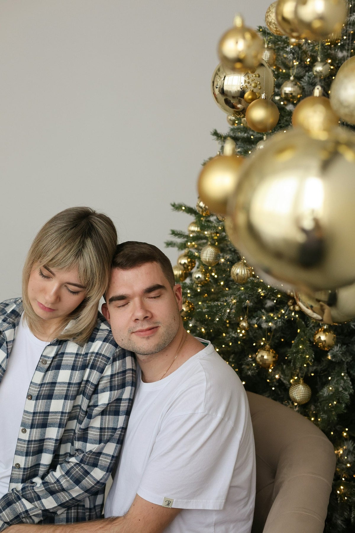 Newlywed couple sitting together by a lit Christmas tree on their first Christmas married